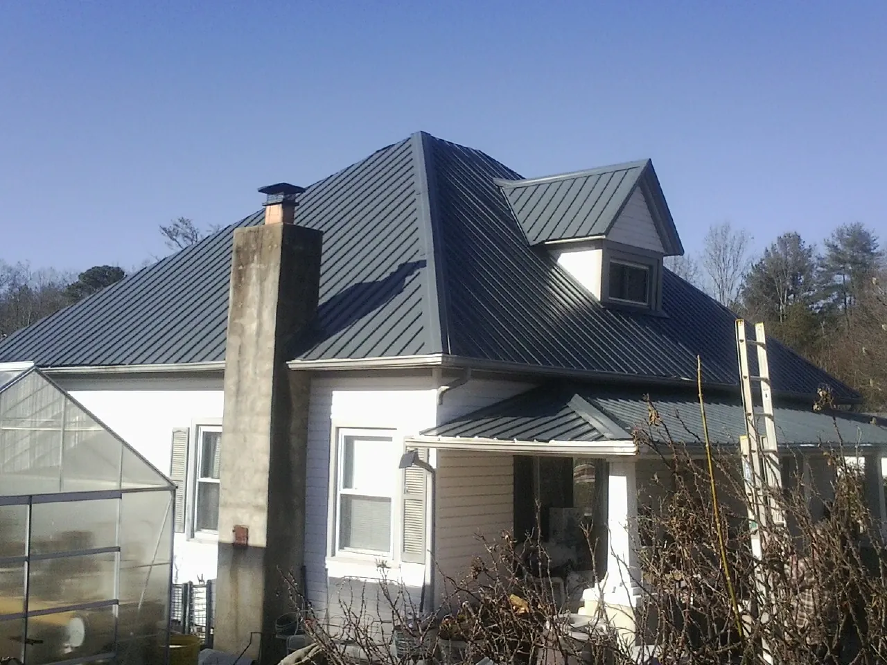 Dark blue standing seam metal roof on a white farmhouse with dormer — Slate & Tile Roof Repair by Roofing Brothers in Rocky