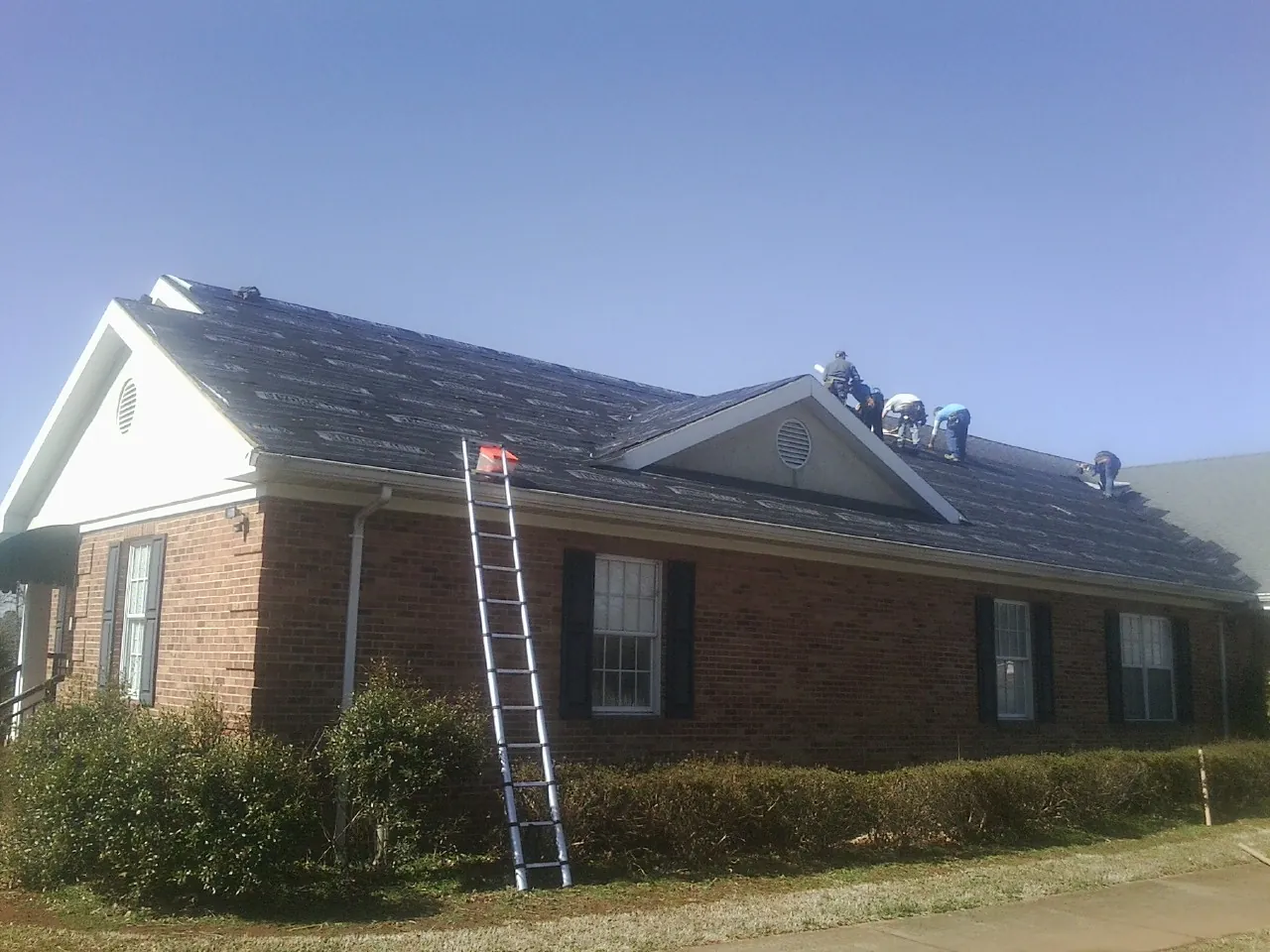 Crew tearing shingles off a brick ranch roof with a ladder set — Metal Roof Repair work by our crew in Rocky
