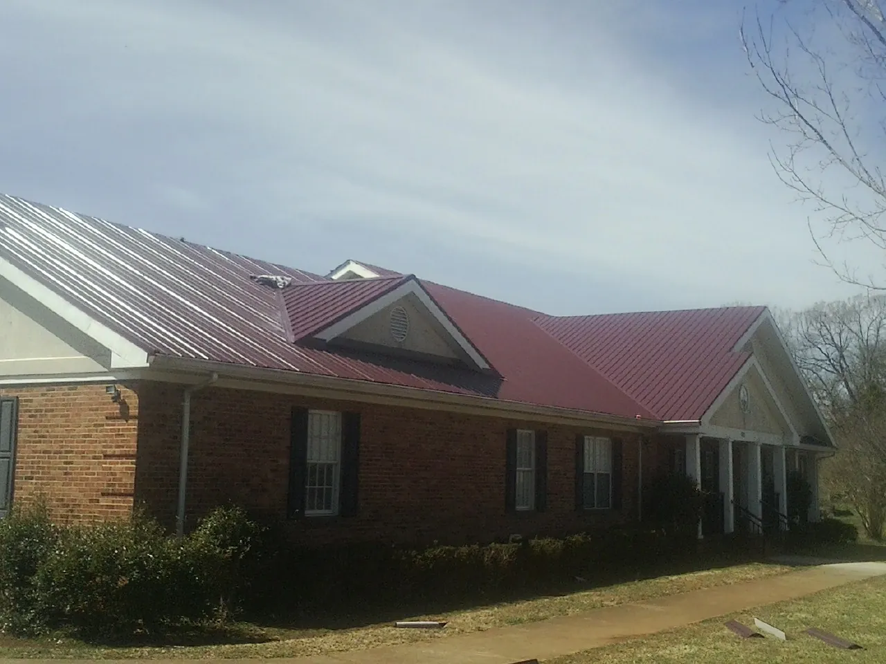 Red metal roof with gabled entries on a long brick building, from a Hail Damage Roof Repair job in Rocky
