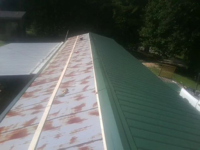 Old rusted panels beside newly installed green metal roofing — Wind Damage Roof Repair by Roofing Brothers in Rocky