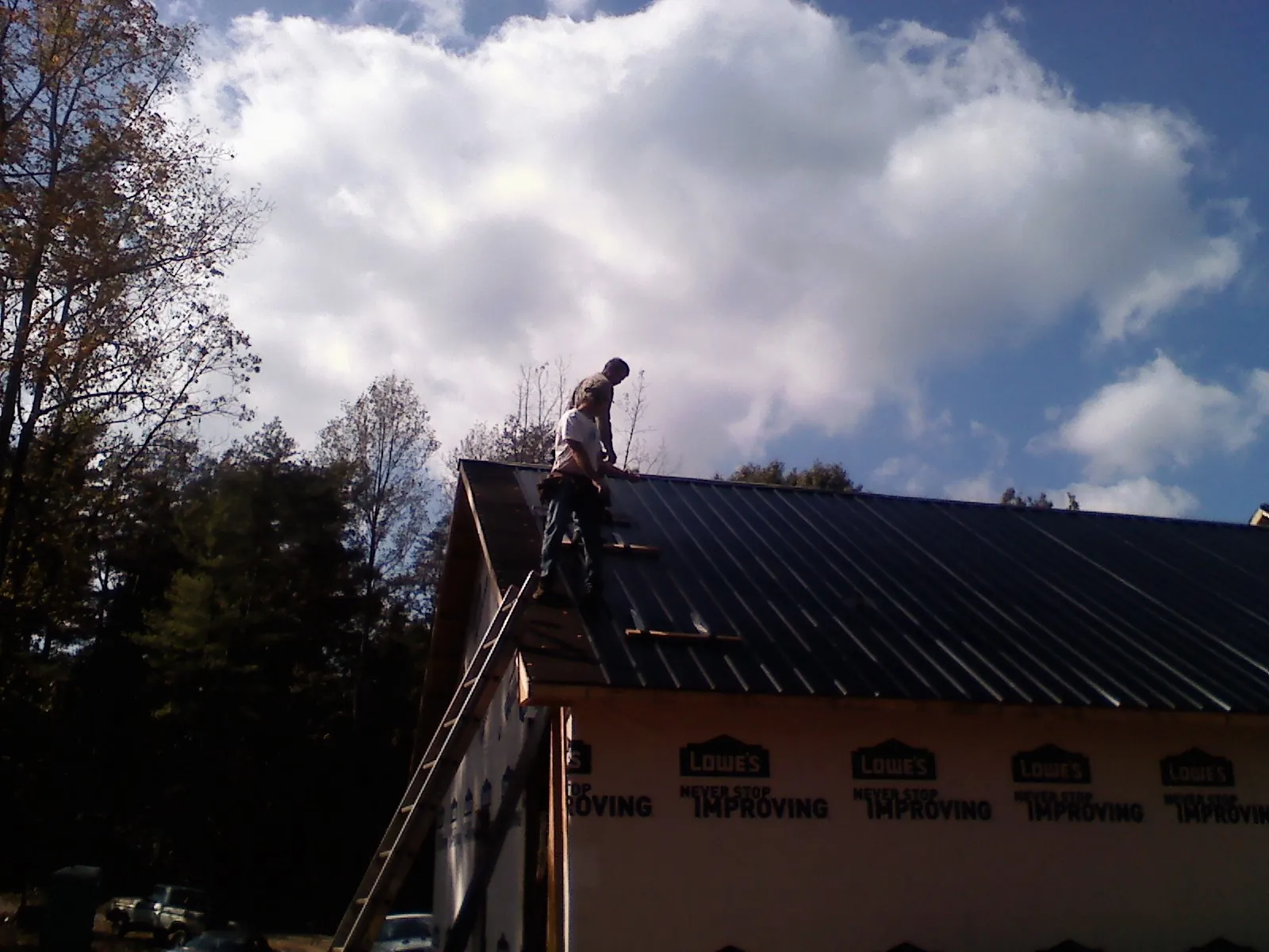 Roofer fastening dark metal panels high against a cloudy sky, from a Roof Inspection job in Rocky