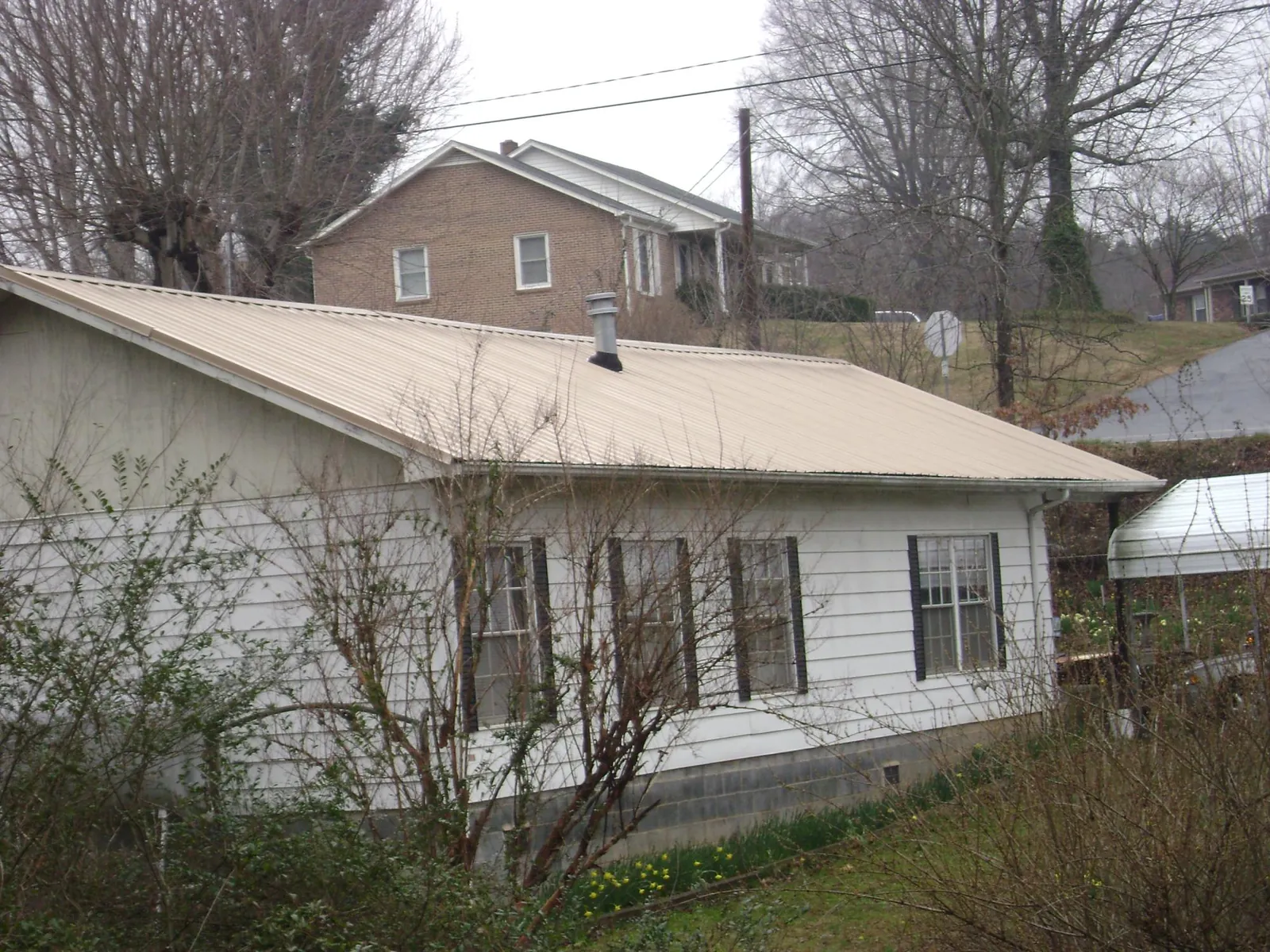 Tan metal roof on a white sided house set into a hillside — Commercial Roofing by Roofing Brothers in Rocky