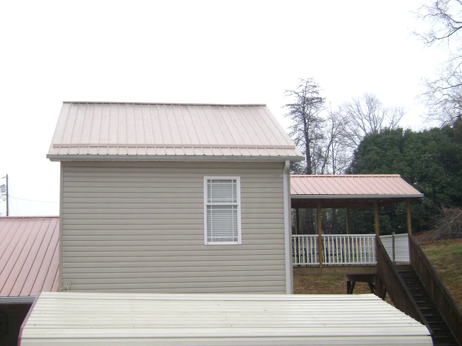Tan metal roofs on a two story addition and attached porch, from a Roof Replacement job in Rocky