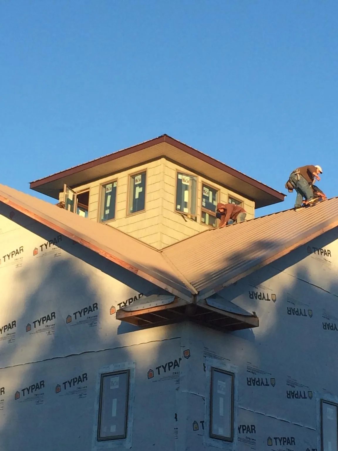Roofers working around a rooftop cupola on a new metal roof at sunset — Roof Waterproofing in Rocky by Roofing Brothers